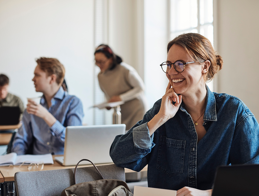 A young woman with glasses smiles while looking off to something on her right. 