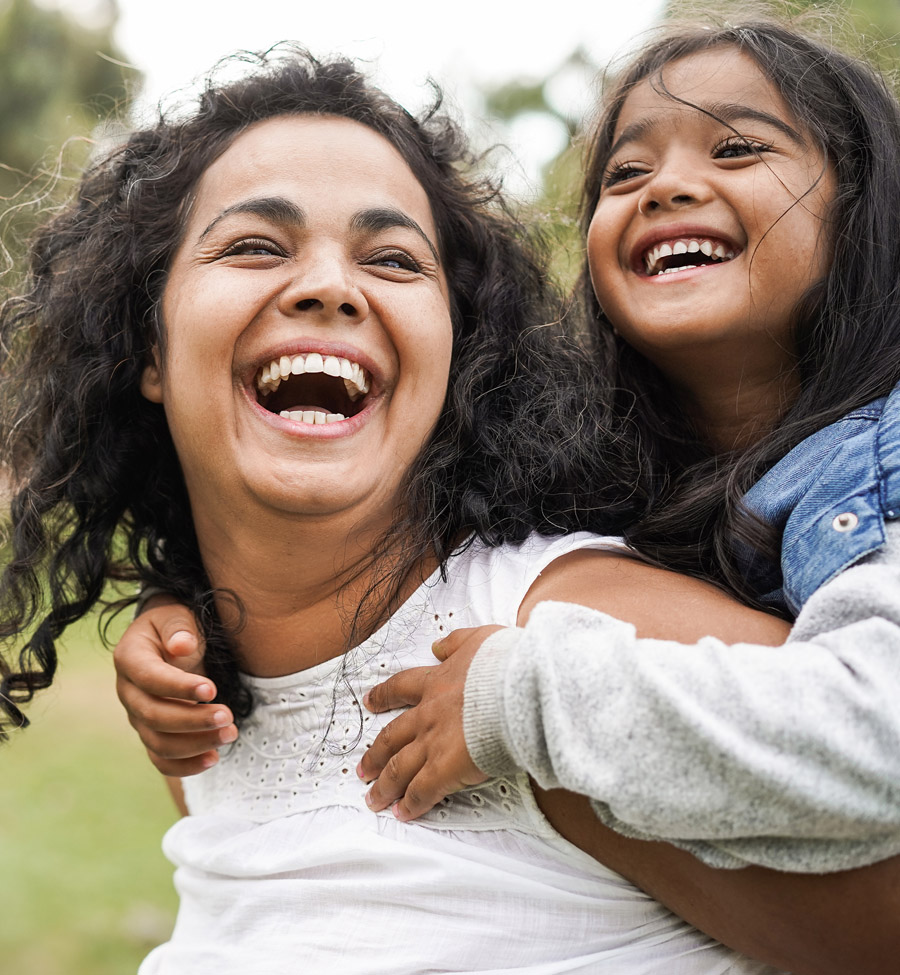 Mother and young daughter laughing outdoors