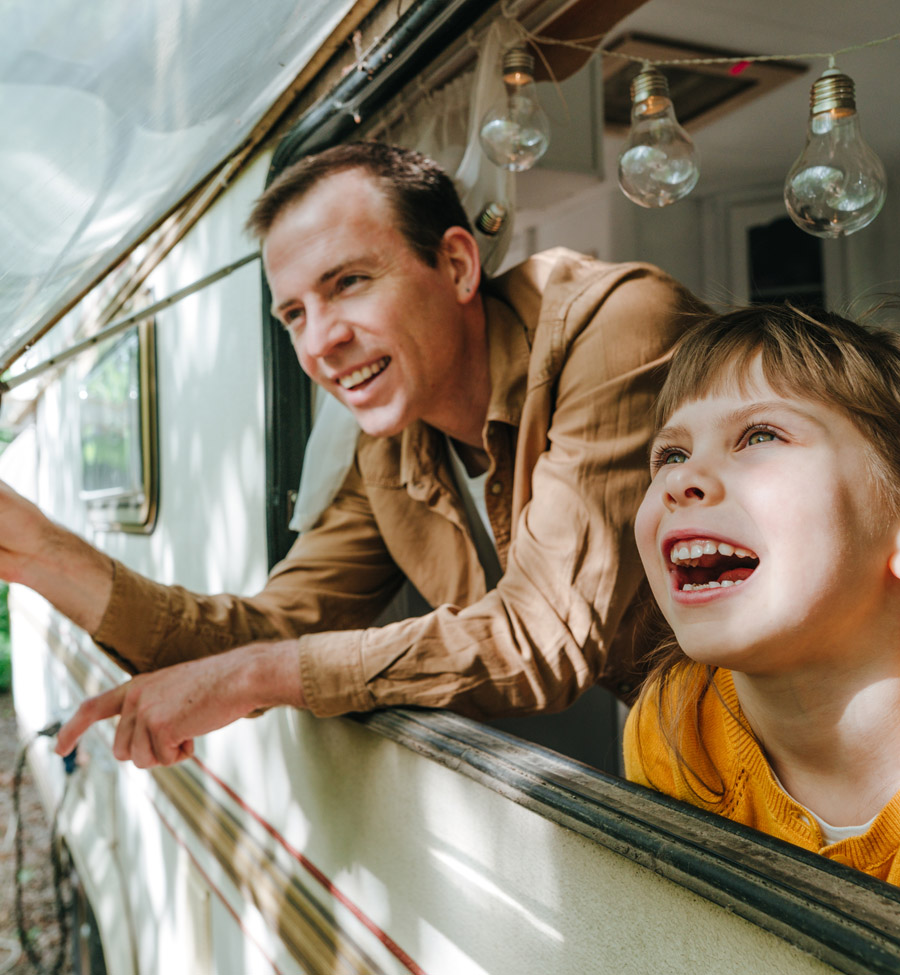 Father and daughter joyfully peeking out camper window