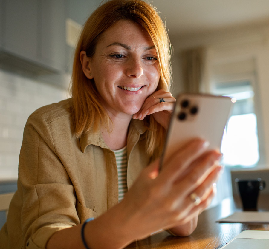 Woman holding mobile phone while sitting in kitchen