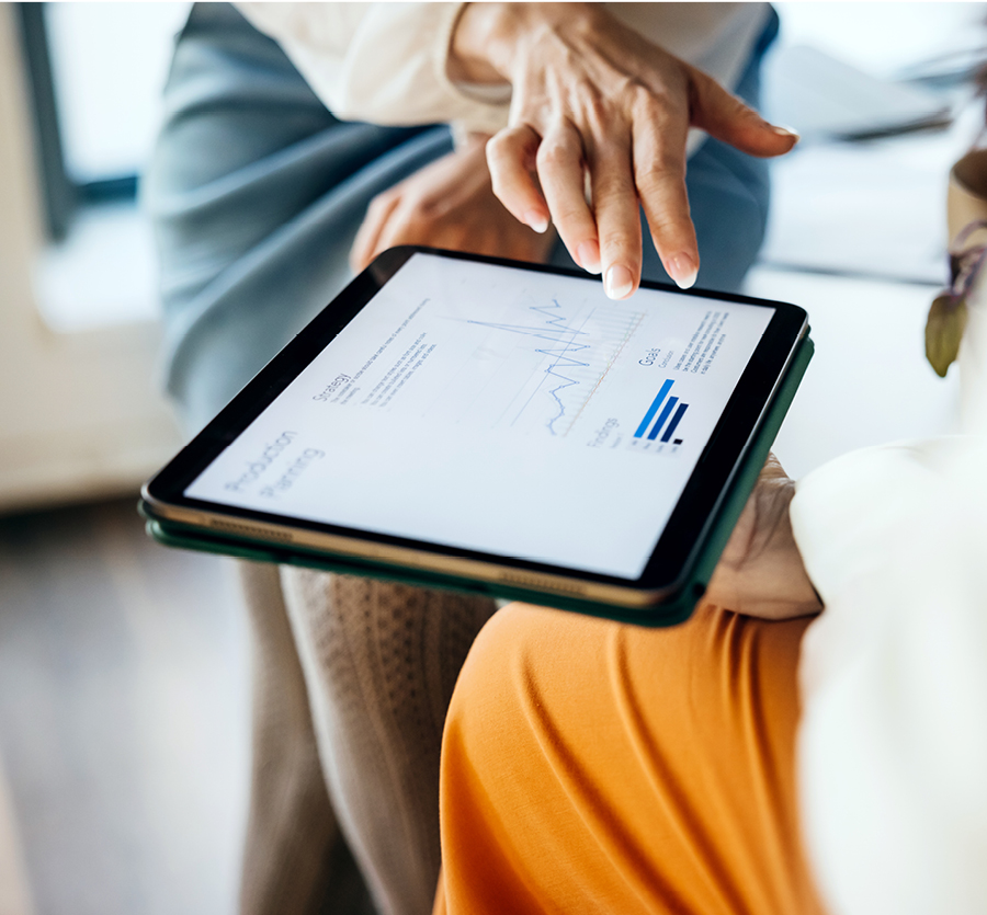Two women look at charts and data on a shared tablet. 