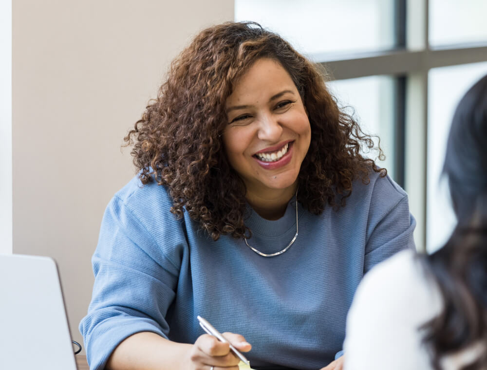 Woman with curly hair in blue sweater smiles at a colleague