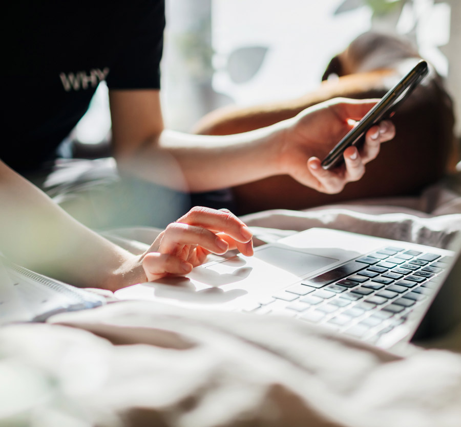 Young adult on computer and holding mobile phone