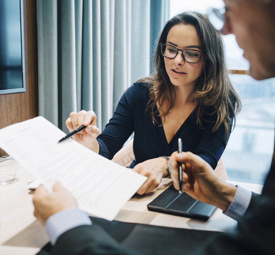 Two people reviewing a business document together. Woman uses a pen to point at something on page.