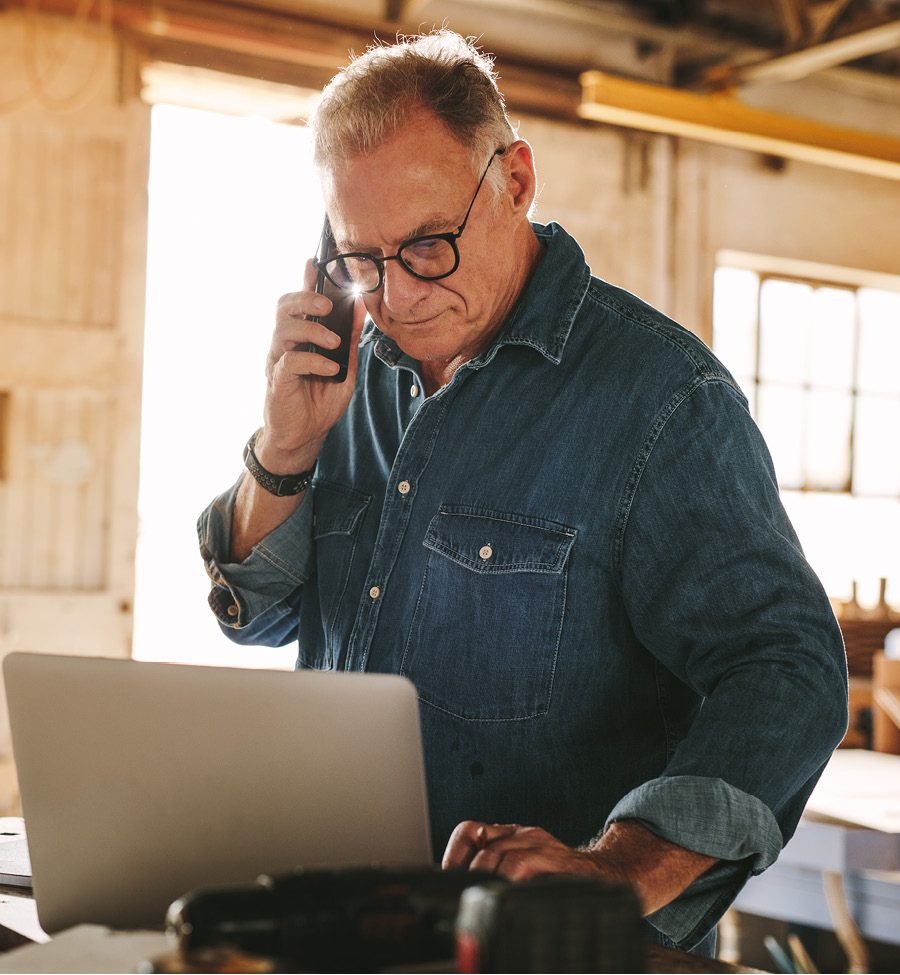 Mature man in shop looking at computer and talking on phone