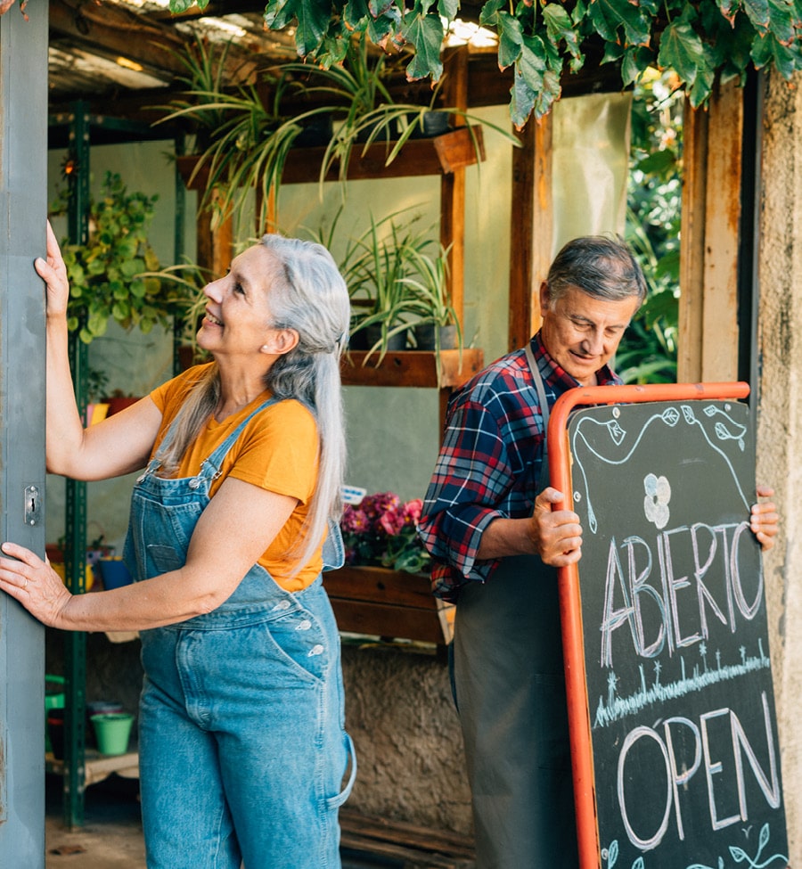 Older couple opens doors to plant shop and places "OPEN" sign out front.