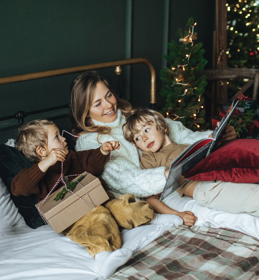 Mother reading books to sons in a cozy bed at Christmas time.