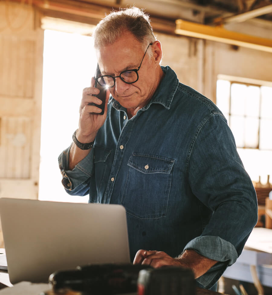 Mature man in shop looking at computer and talking on phone