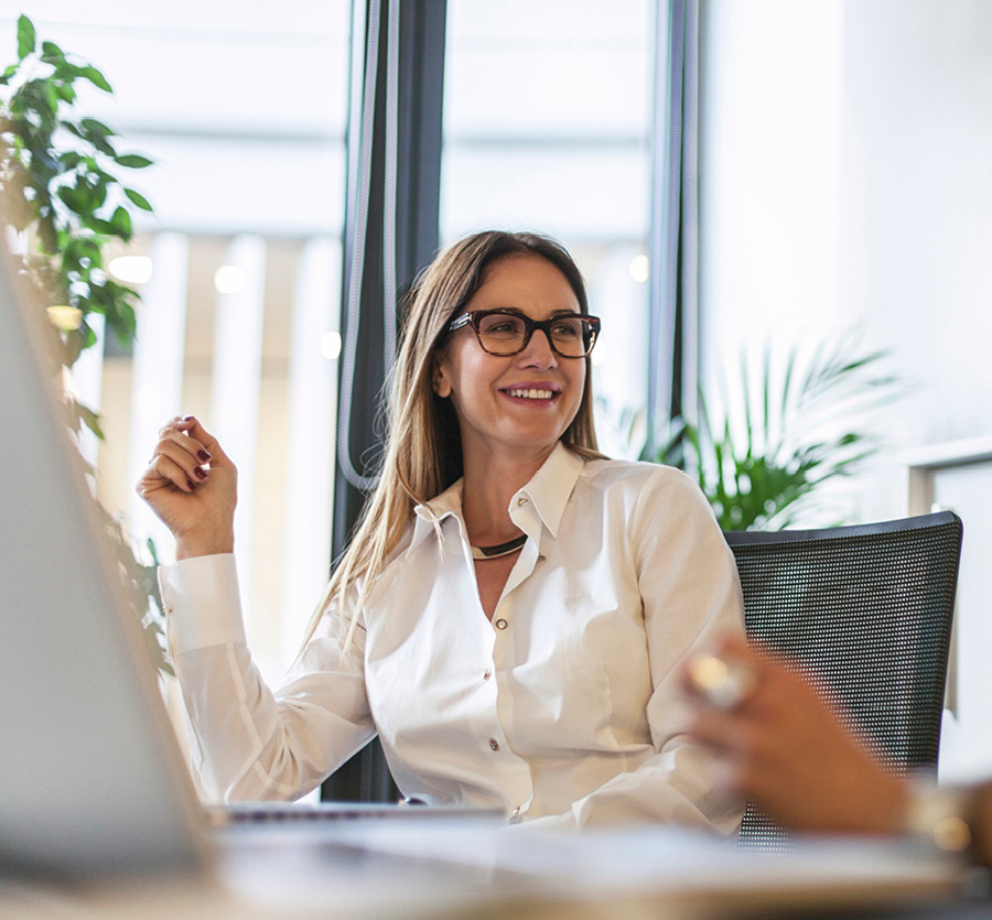 A woman sitting in an office, smiling at a colleague out of frame.