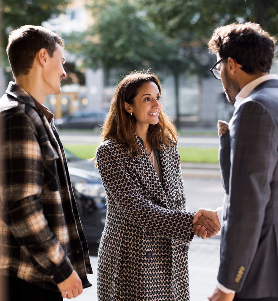 A woman stands with two men, shaking hands with one of them.