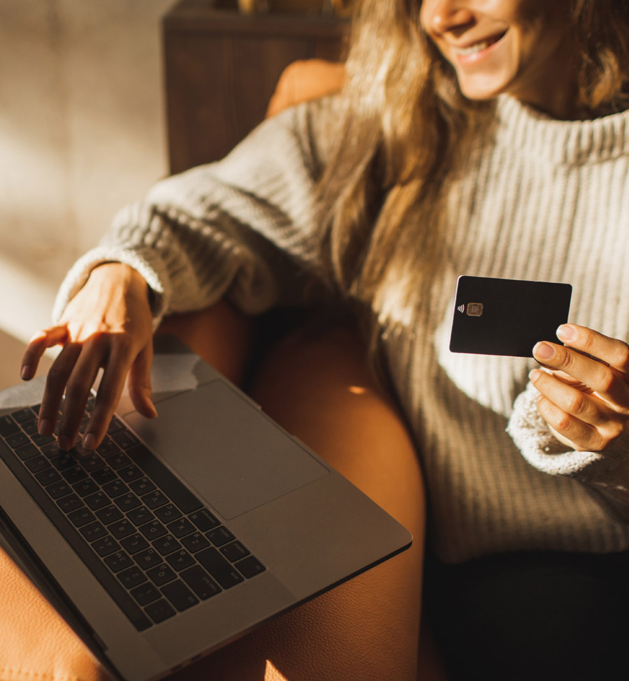 A woman types on laptop, holding a credit card in the one hand.