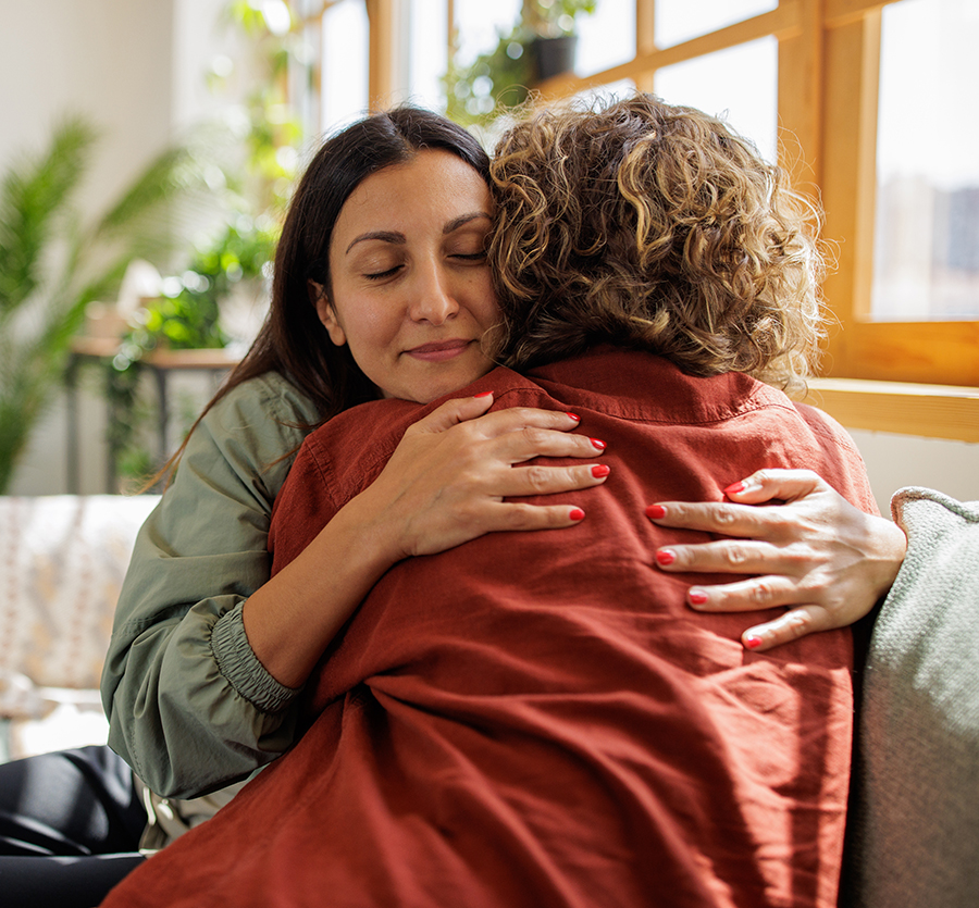 Two women hugging on a couch, offering care and support.