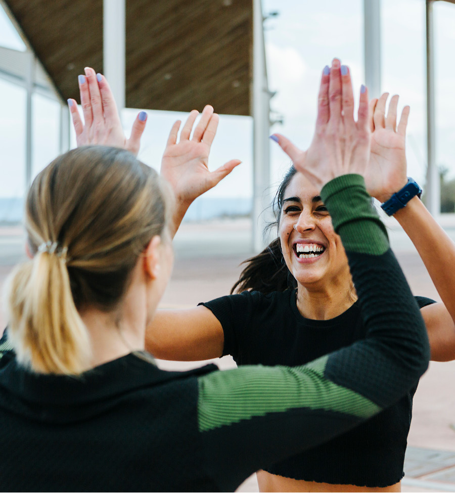 Two smiling women exchange an encouraging high-five outdoors.