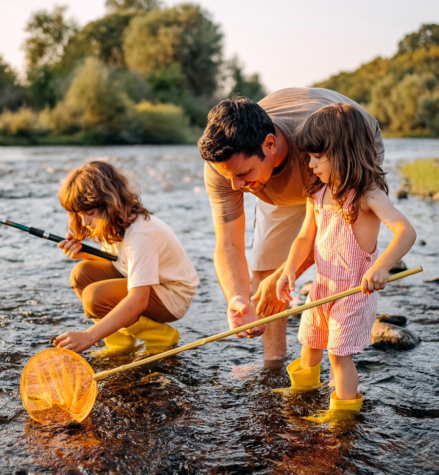 A dad and two young daughters fishing in a shallow creek with nets.