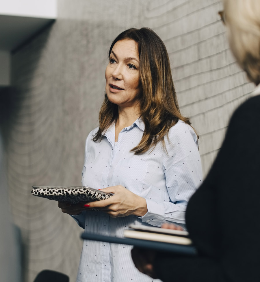 A woman in conversation with other women, all holding notebooks.