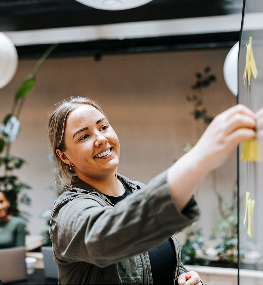 A woman stands at a white board moving yellow sticky notes.