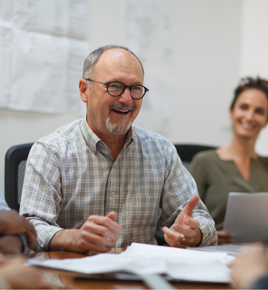 A man engaged in a meeting with others, smiling and gesturing lightly with hands.