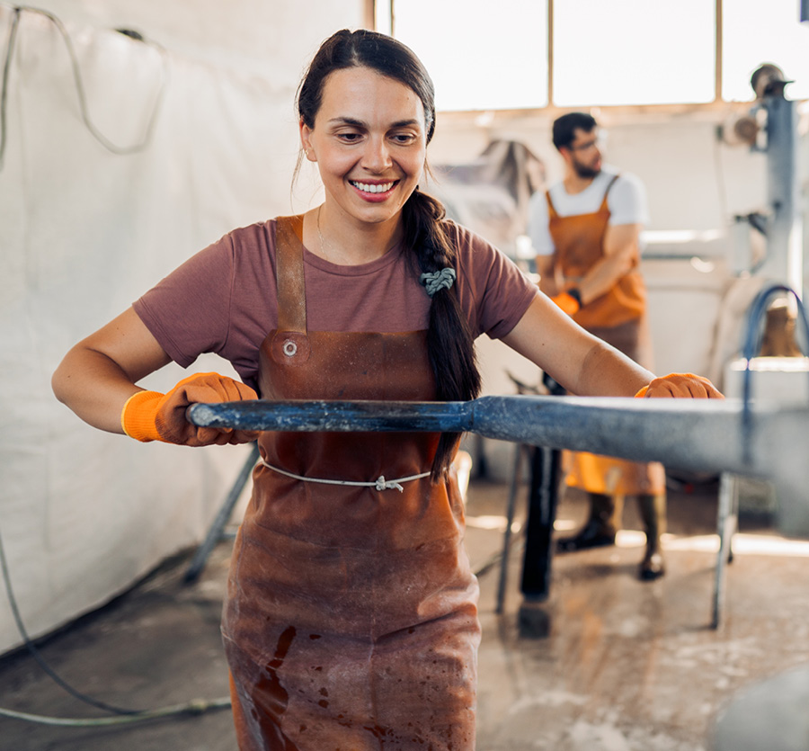 A smiling woman in a factory operates an arm to a machine.