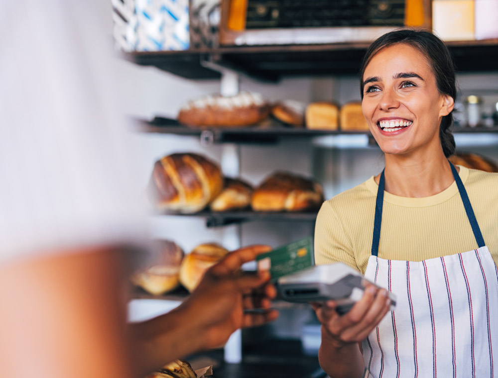 A female employee at a bakery collects payment from a customer.